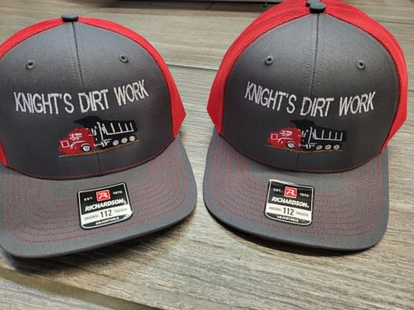 Gray and red trucker hats embroidered with the Knight's Dirt Work dump-truck logo