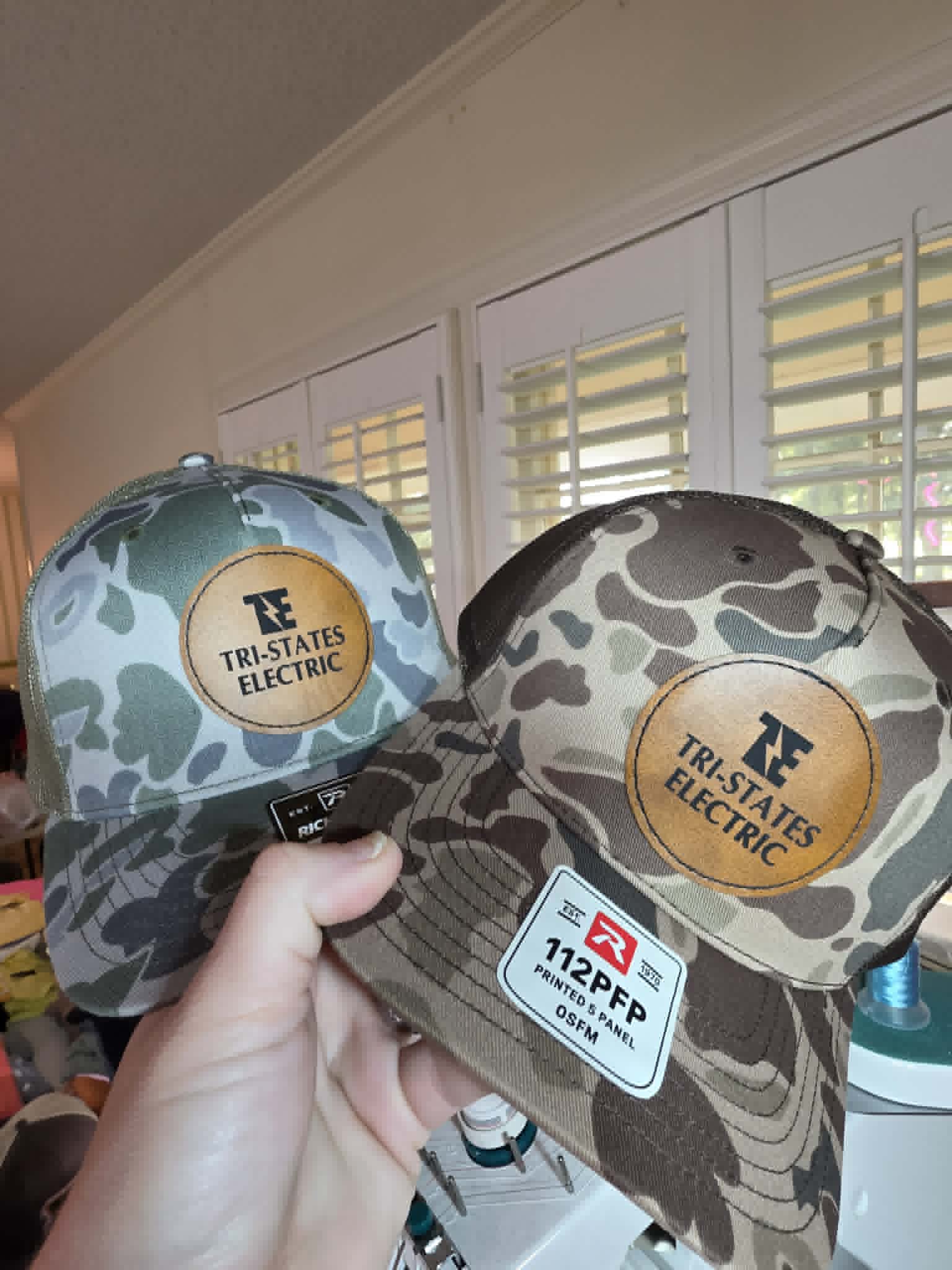 Two camouflage trucker hats with round Tri-States Electric leather patches