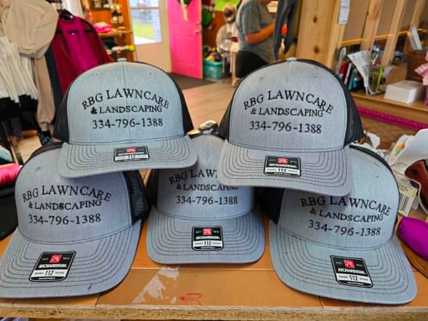 Gray and black trucker hats embroidered with RBG Lawncare and Landscaping contact details