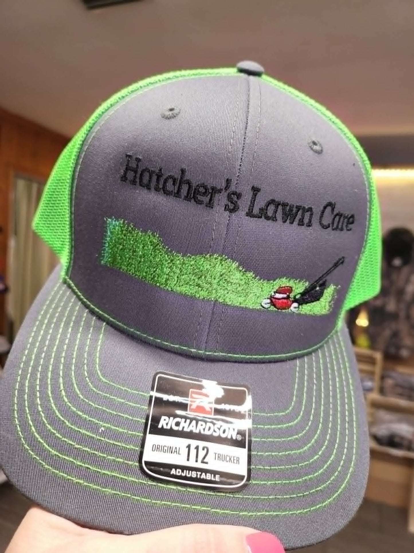 Gray and neon-green trucker hat embroidered with Hatcher's Lawn Care and mower graphic