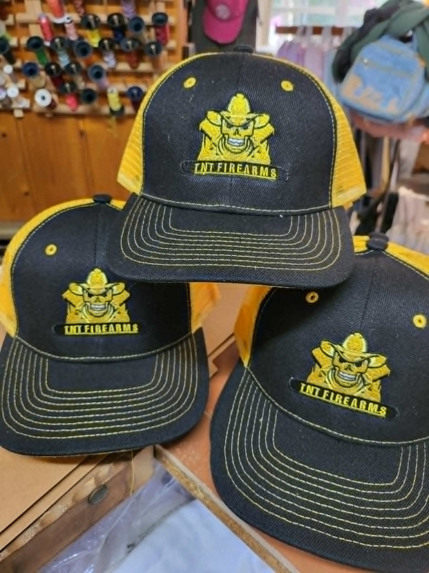 Black and yellow trucker hats embroidered with the TNT Firearms cowboy logo