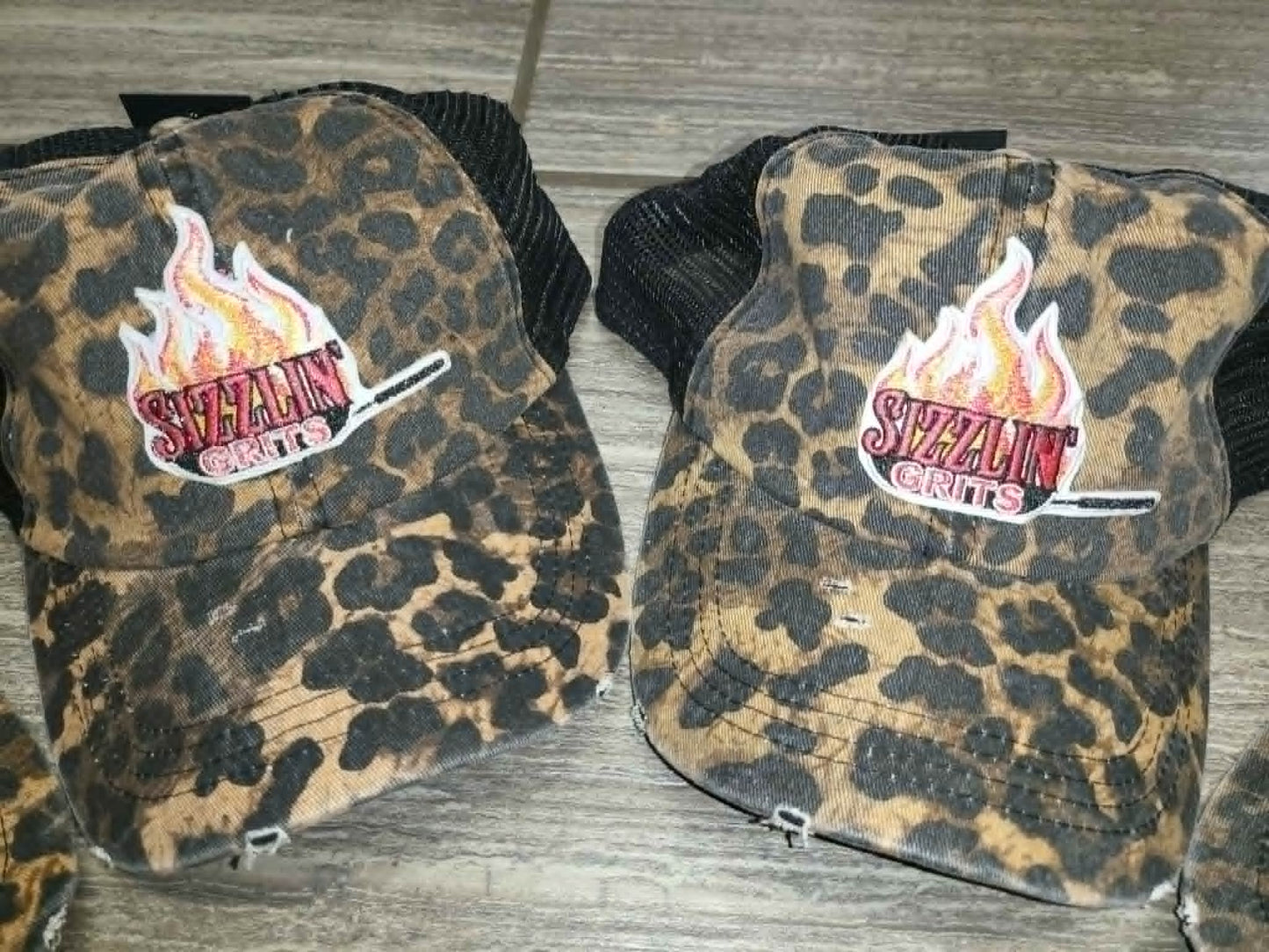 Patterned brown and black trucker hats with colorful Sizzlin' Grits skillet logos