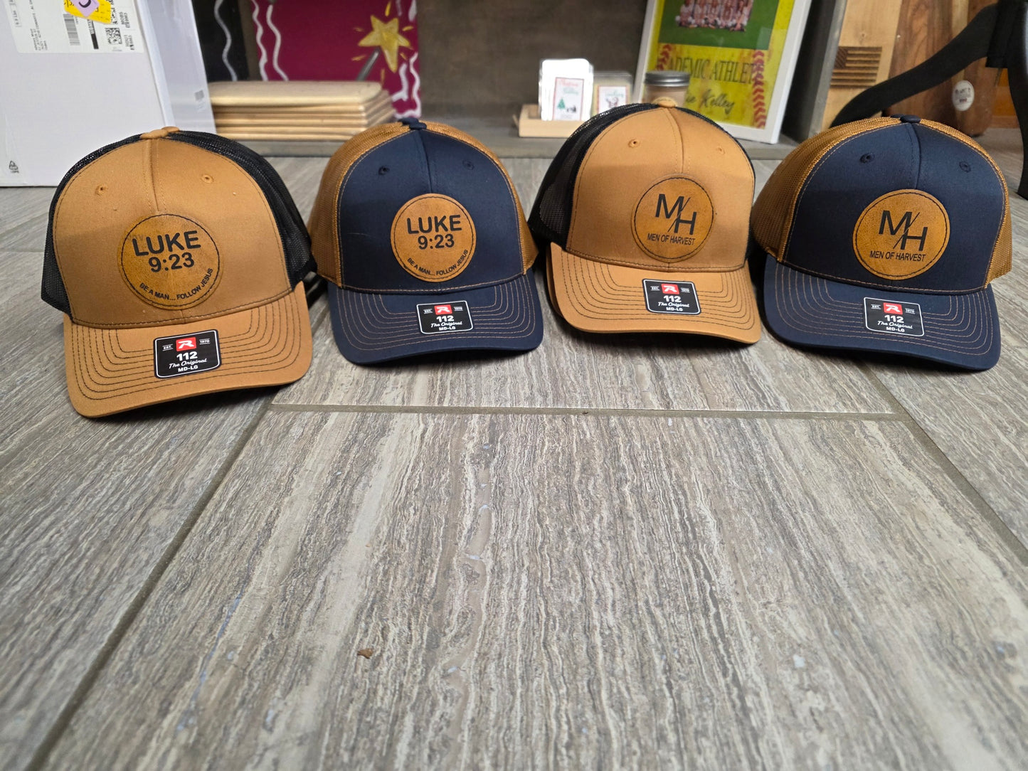 Brown and navy trucker hats with Luke 9:23 and Men of Harvest round leather patches